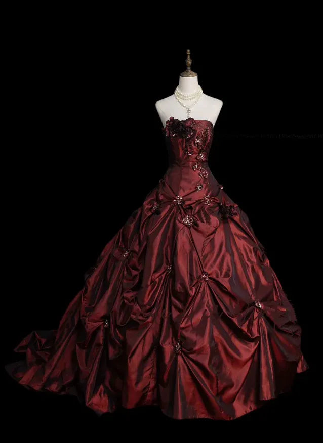 Model wearing a burgundy strapless satin ball gown with floral appliques.