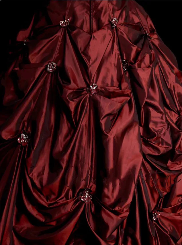Model posing elegantly in the floor-length burgundy strapless evening dress.