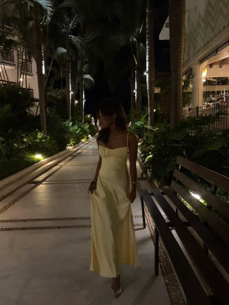 Woman wearing a butter yellow satin A-line maxi dress with spaghetti straps and ruched bust detail.