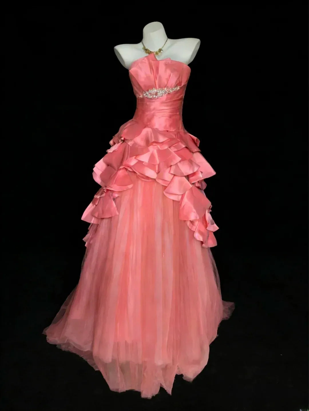 Full view of a coral pink strapless sweetheart ball gown with a ruffled tulle skirt and rhinestone waist.