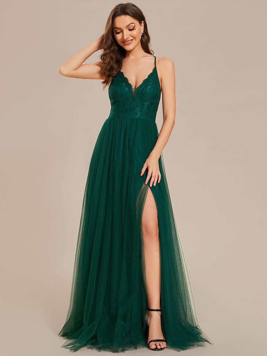 Model wearing a dark green A-line tulle bridesmaid dress with lace top, spaghetti straps, and a high slit.