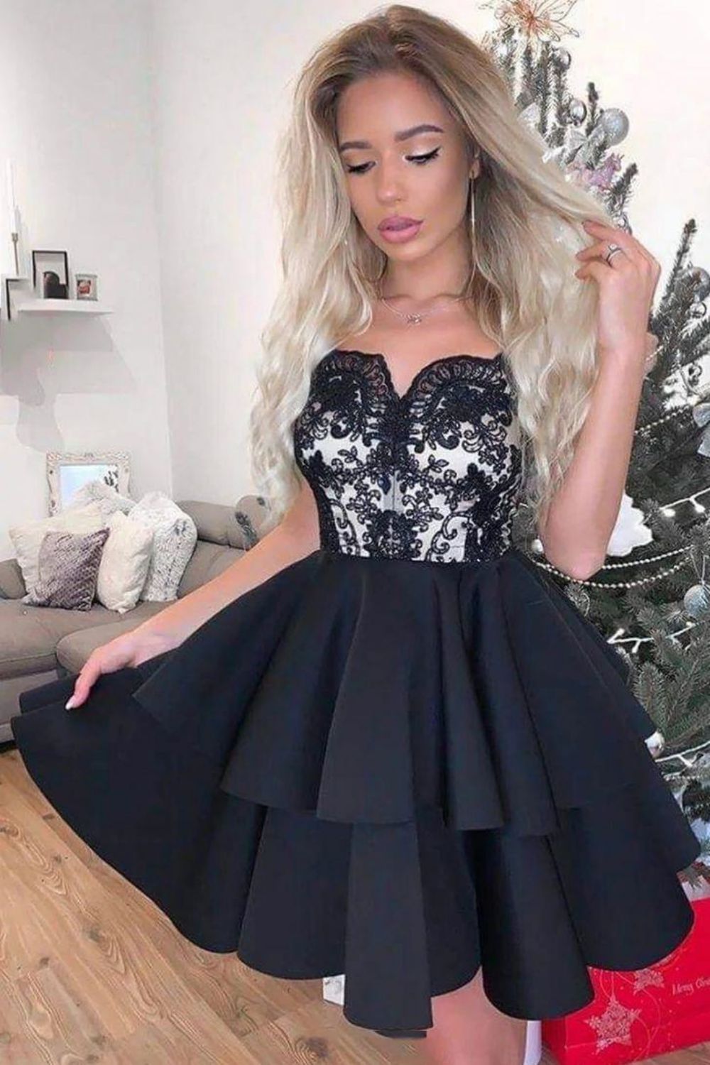 Model wearing a black mini homecoming dress with intricate applique details and a high neckline.