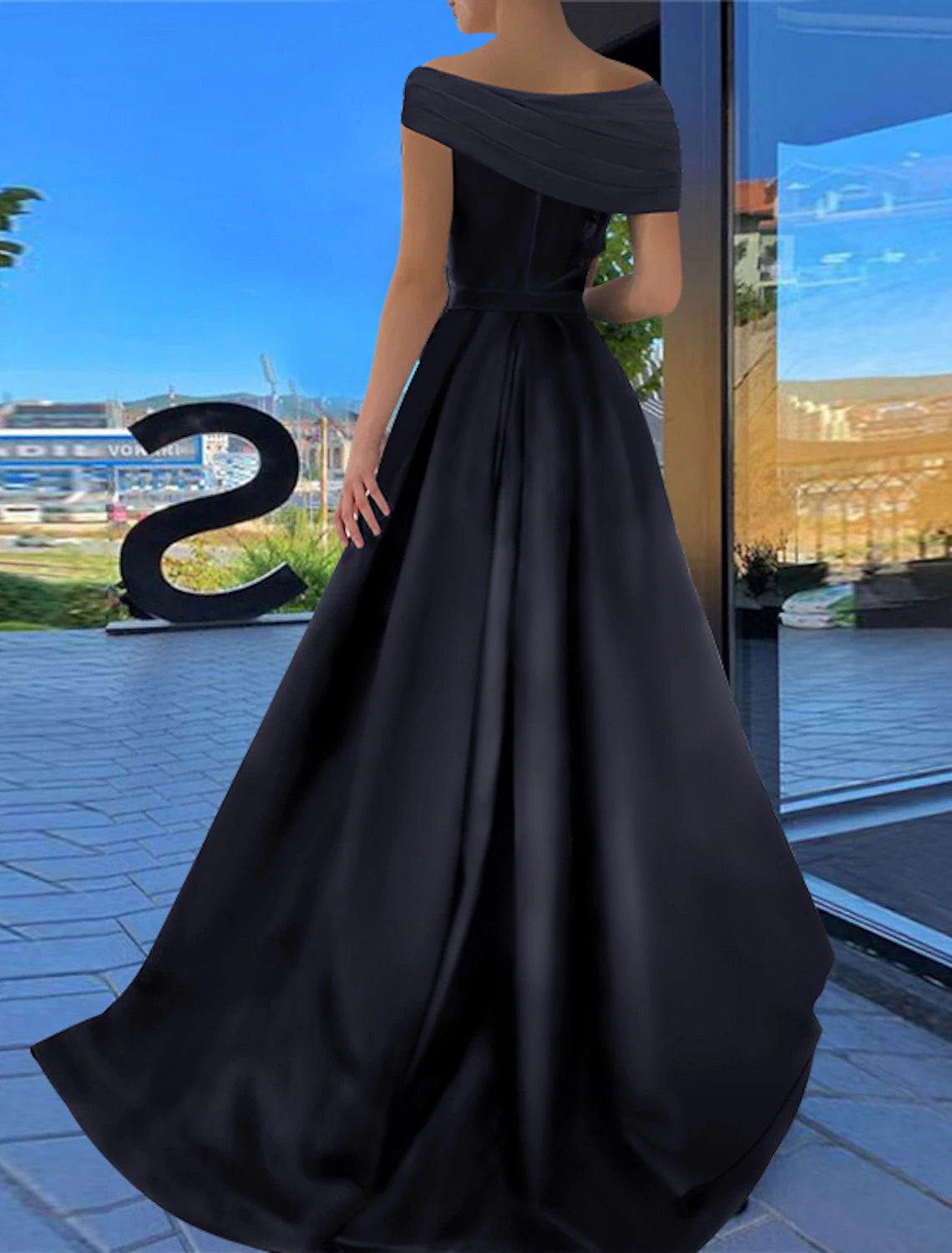 A woman in a black off-shoulder satin A-line dress with a ruched slit, shown from a different angle.