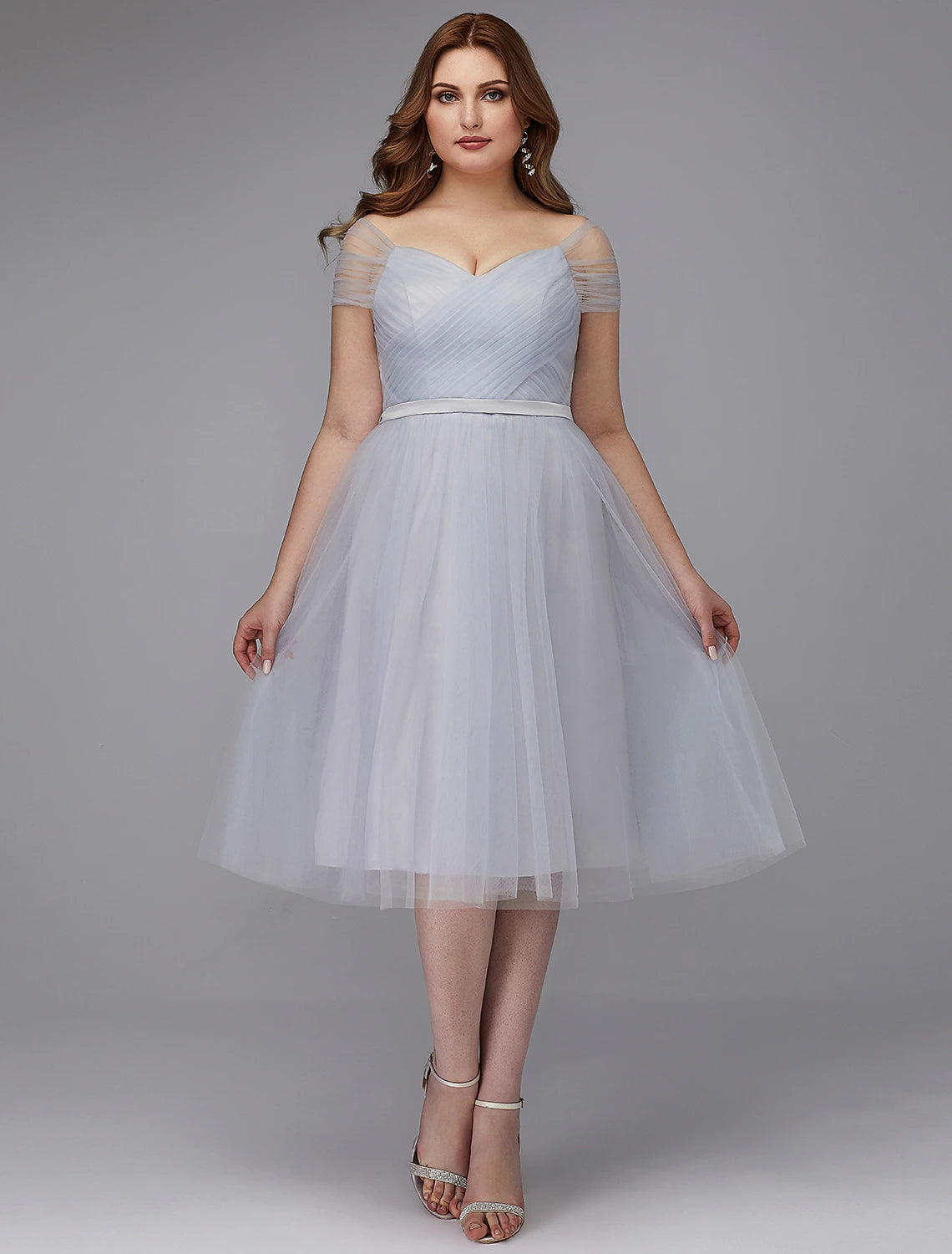 Model wearing an elegant off-shoulder A-line tulle dress with short sleeves and a sash, tea length.
