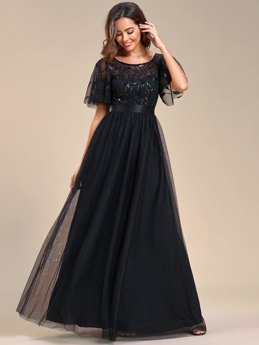 Woman wearing a black A-line short sleeve embroidered floor length evening gown, posing elegantly.