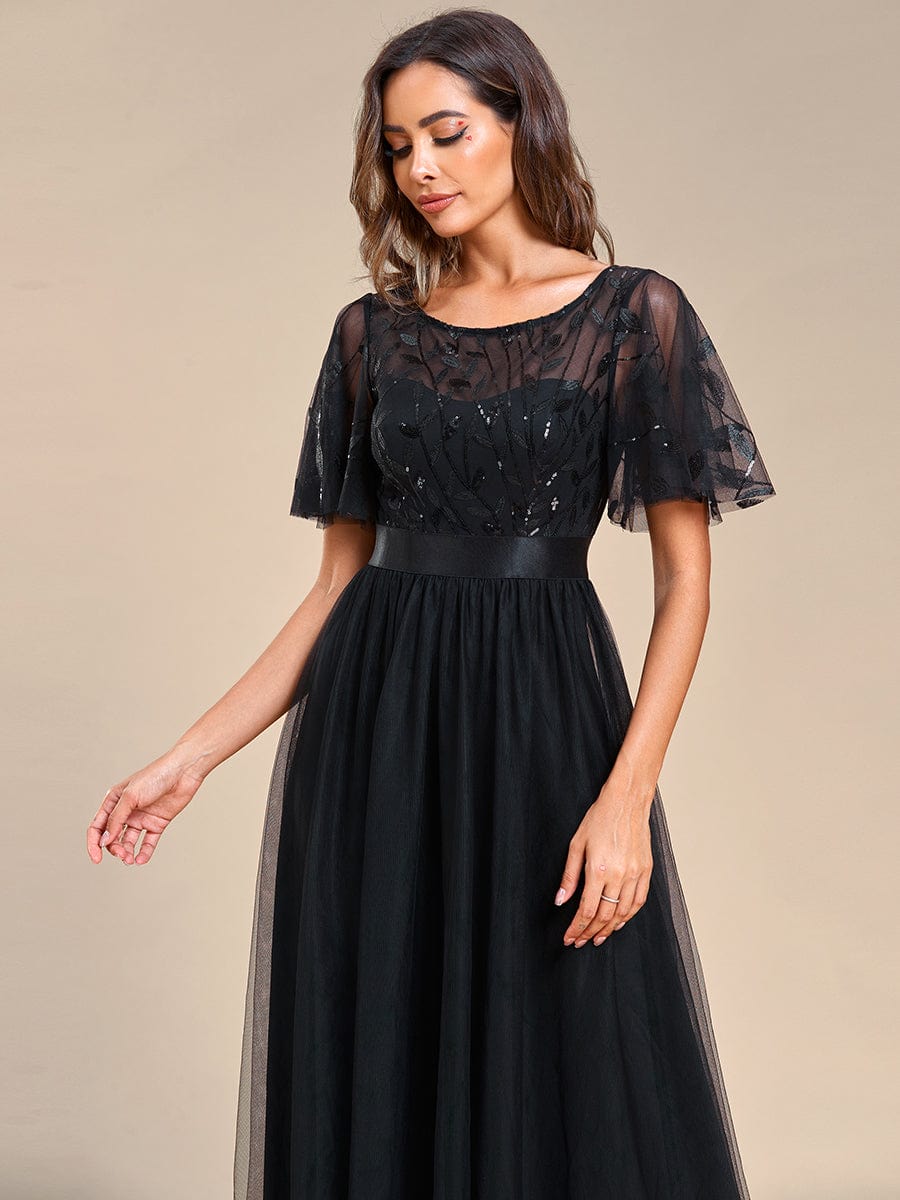 Woman in a black A-line short sleeve embroidered evening gown, standing gracefully.