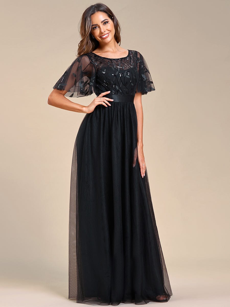 Side profile of a woman wearing a black A-line short sleeve embroidered evening gown.