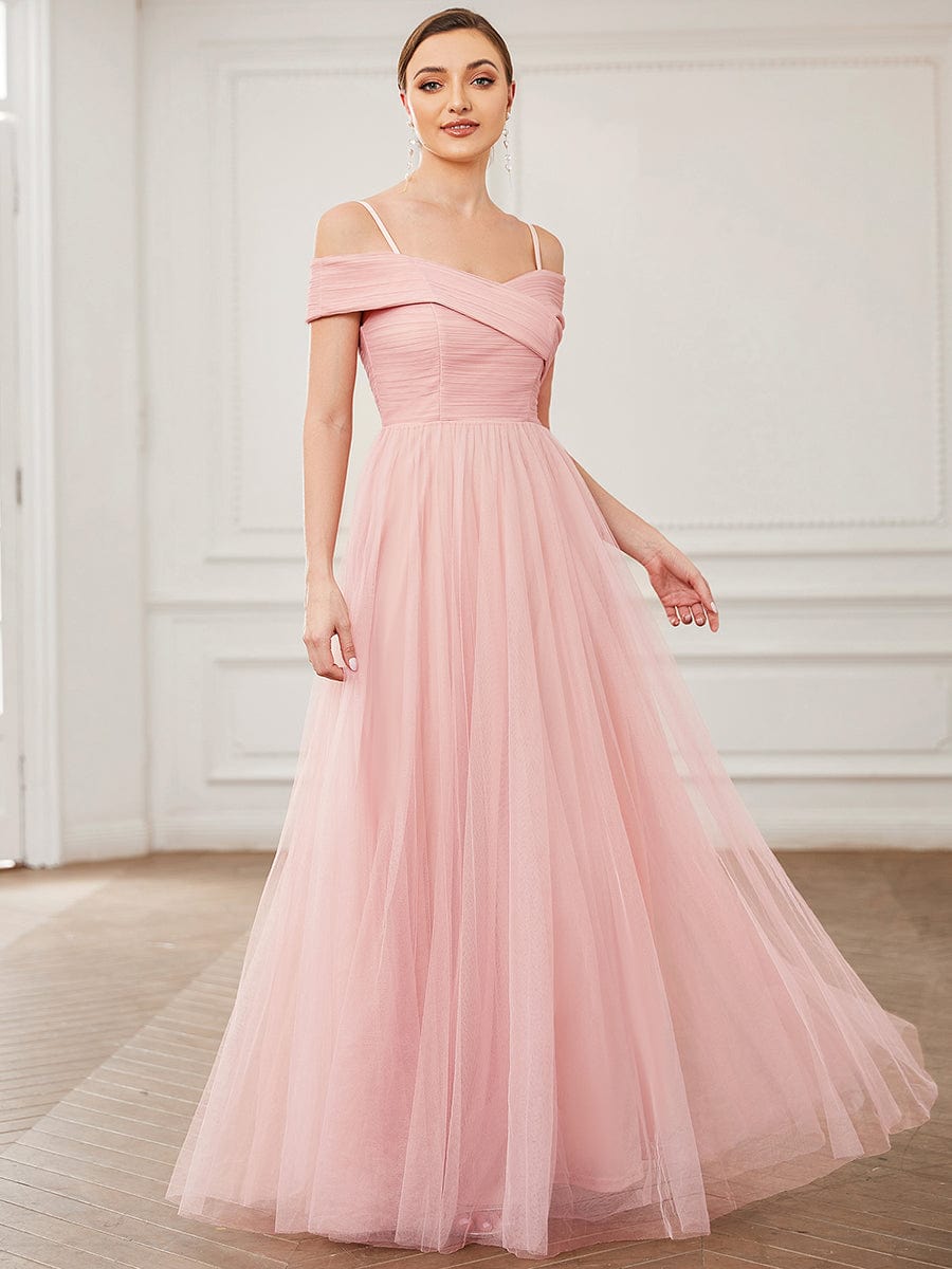 Model in a pink A-line tulle bridesmaid dress with spaghetti straps and cold shoulders.