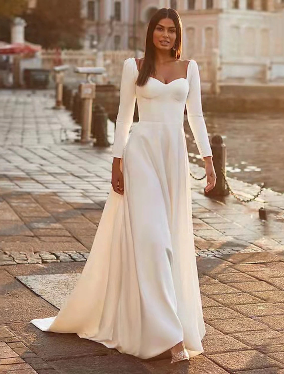 Woman wearing an elegant A-line sweetheart long sleeve satin wedding guest dress with a sweep train, front view.