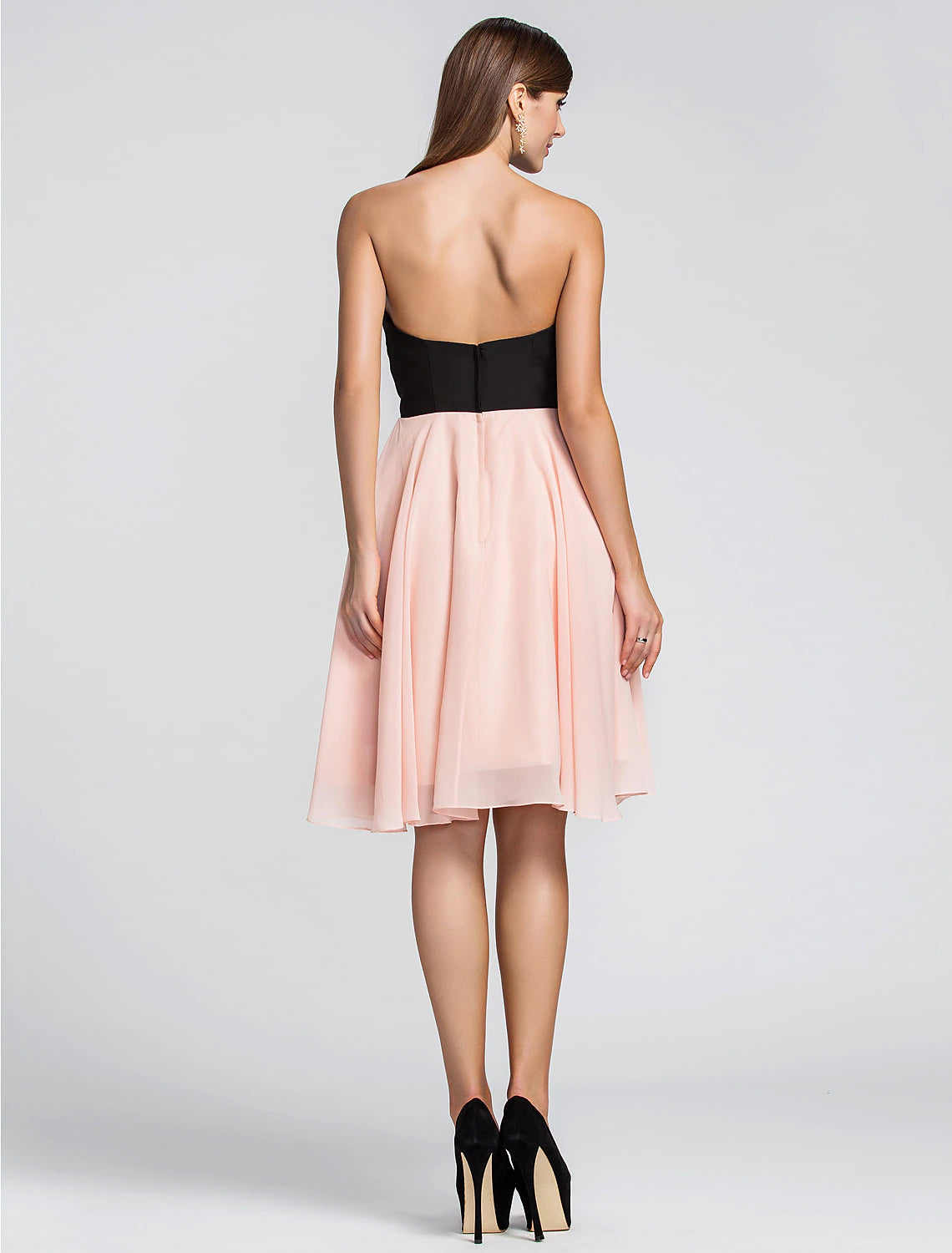Back view of a woman in a knee-length pleated chiffon cocktail dress.
