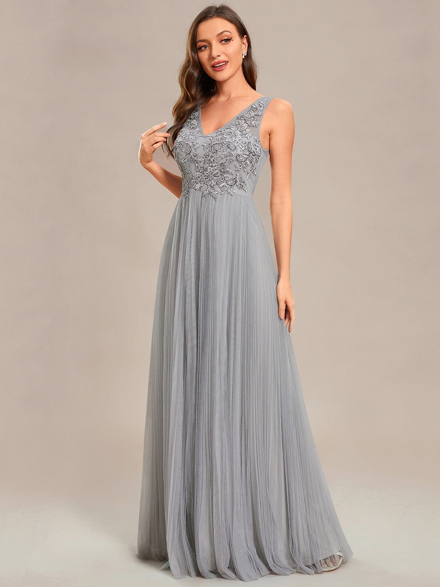 Model wearing a grey A-line tulle evening dress with applique bodice.