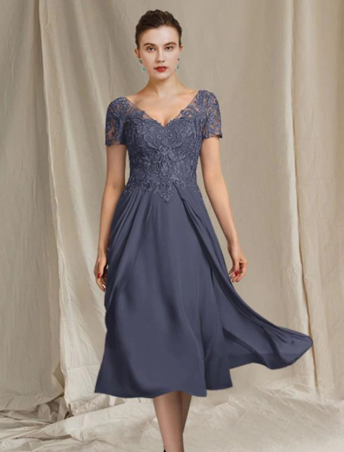 Woman wearing an elegant A-line V-neck tea-length mother of the bride dress with short sleeves and lace details.