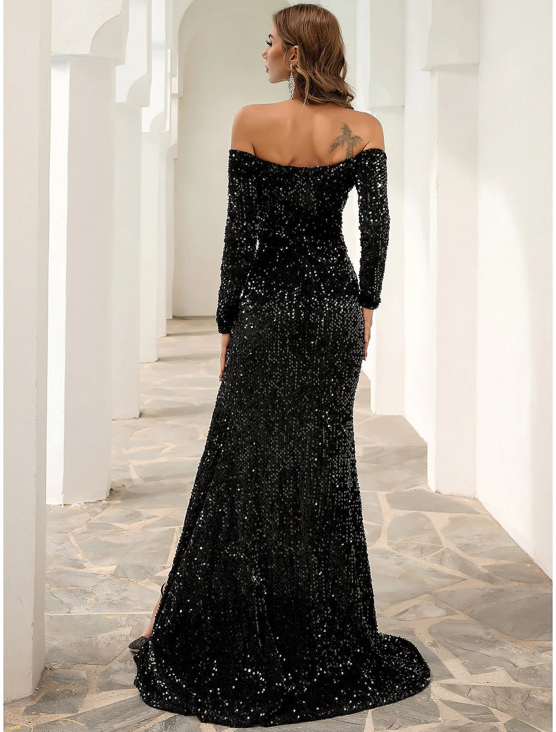 Side view of a woman in a black velvet off-shoulder gown with a sweep train.