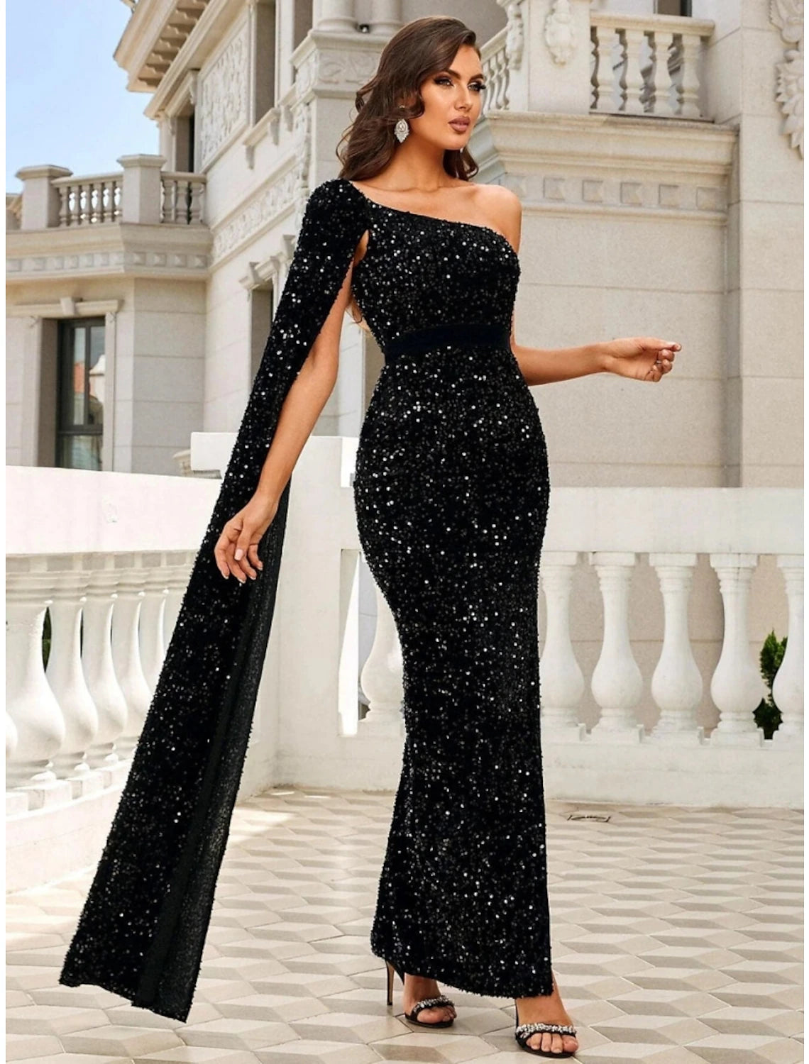 Model posing in an elegant black sequined one-shoulder mermaid trumpet evening gown with a high slit.