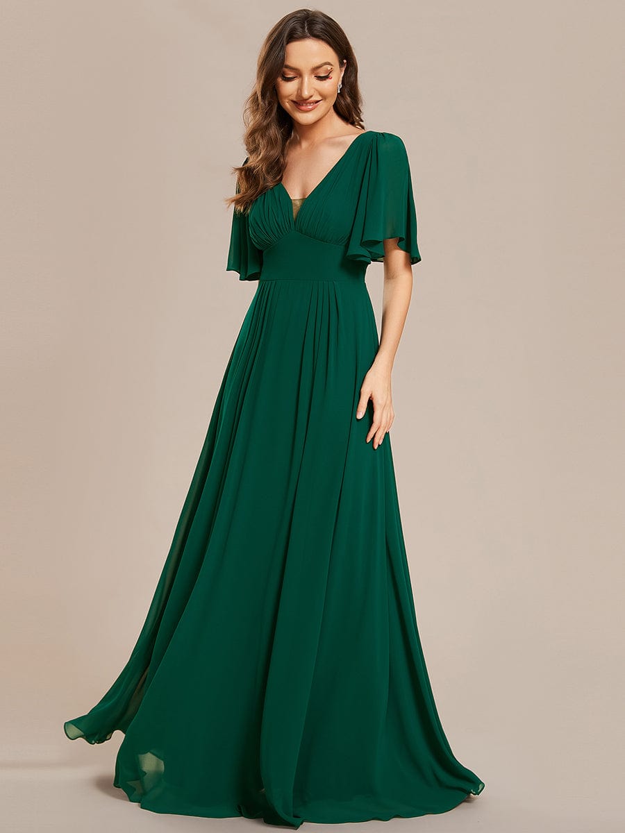 Model wearing a dark green chiffon A-line maxi bridesmaid dress with short sleeves and empire waist.