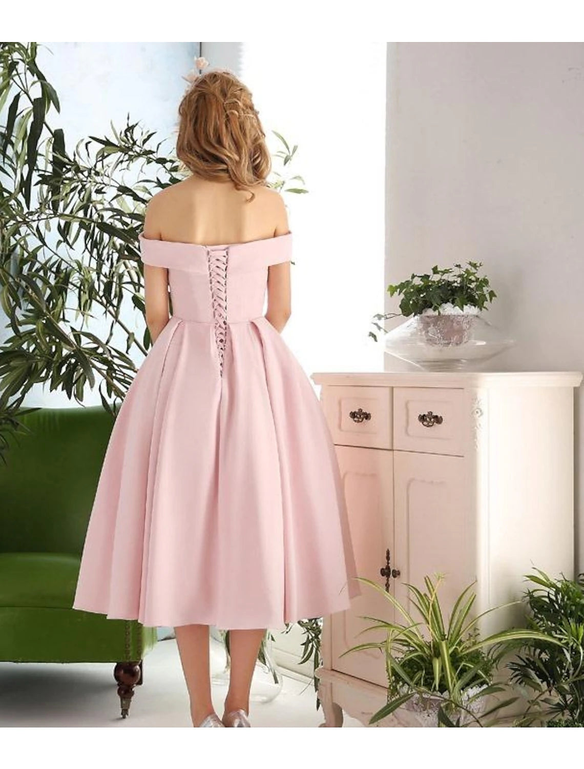 Woman in navy A-line off-shoulder pleated tea-length cocktail dress, back view.