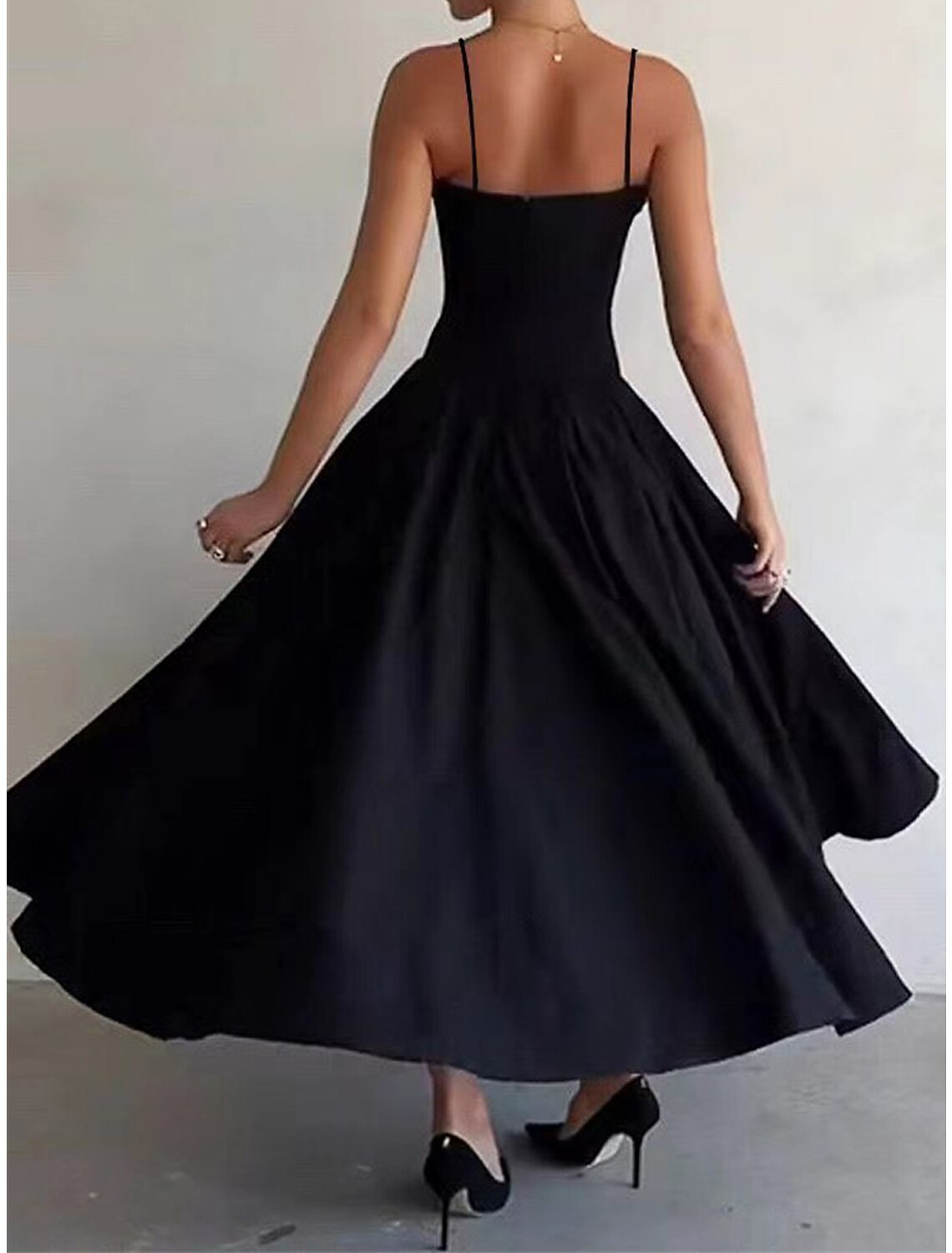 Model wearing a black ruched spaghetti strap maxi dress, side view.