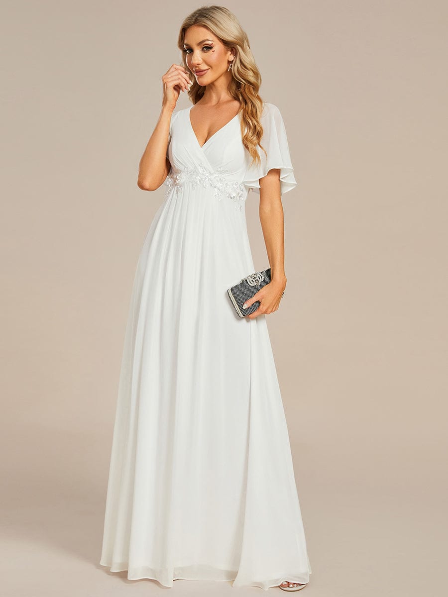 Woman in a cream Weitese A-line chiffon maxi dress with ruffle sleeves.
