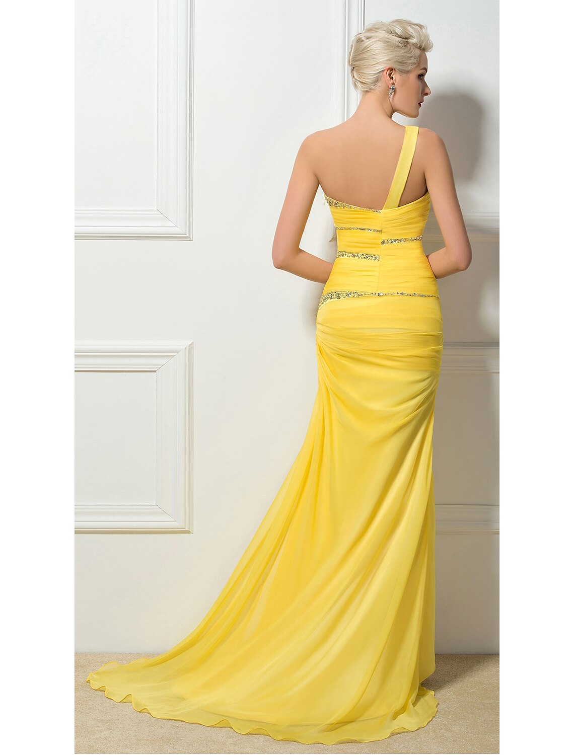 Back view of a woman in a light-colored one-shoulder evening gown, showcasing the backless design and sweep train.