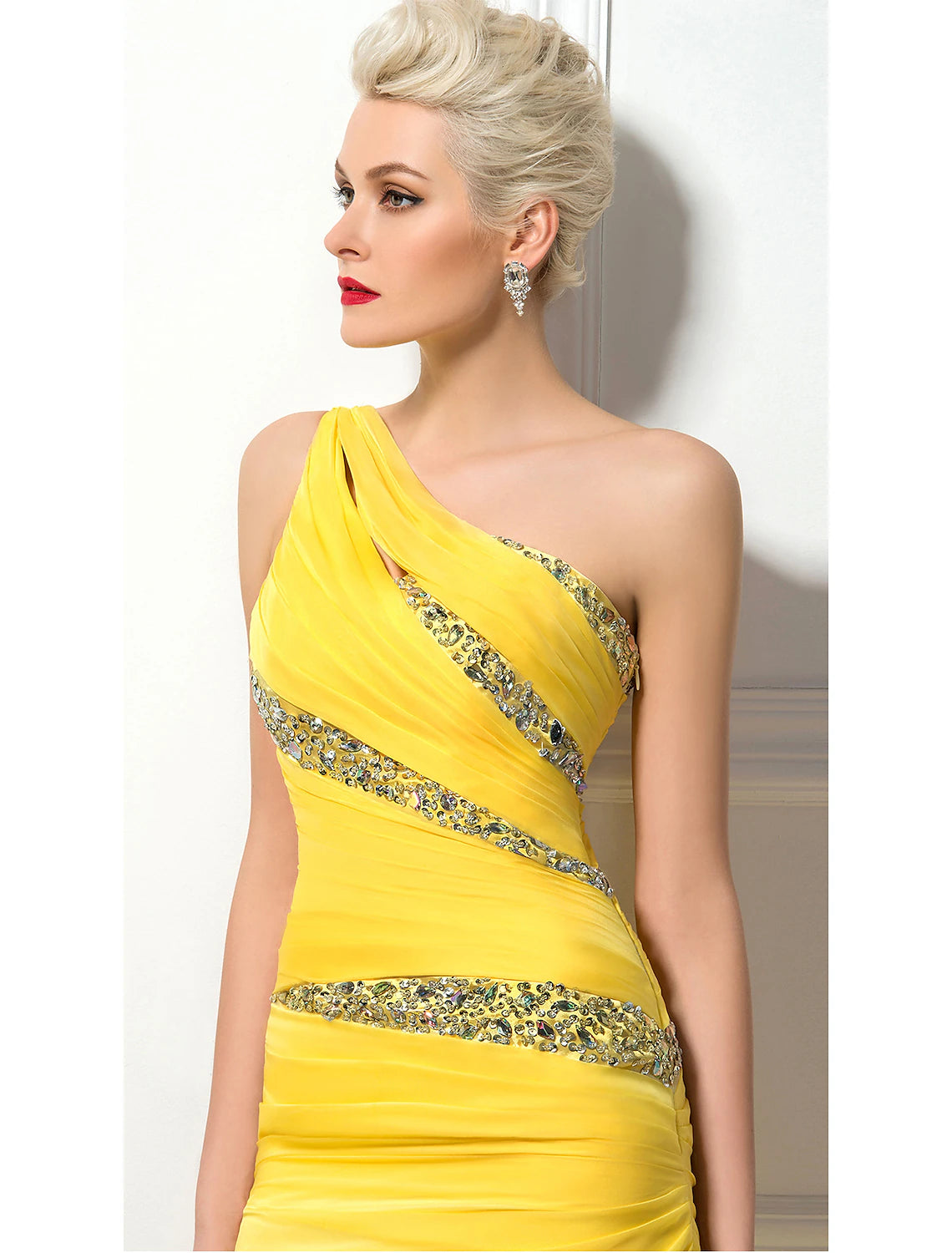 Side profile of a woman wearing a light-colored one-shoulder ruched sequin evening gown.