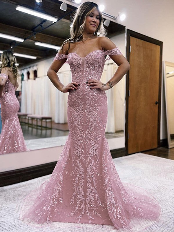 Full-length view of a woman in a light-colored sheath off-the-shoulder lace applique prom dress with a court train.
