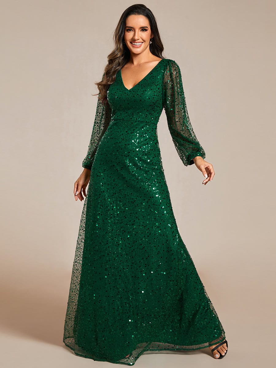 Woman wearing a dark green shimmering sequin A-line evening dress with V-neck and long lantern sleeves.