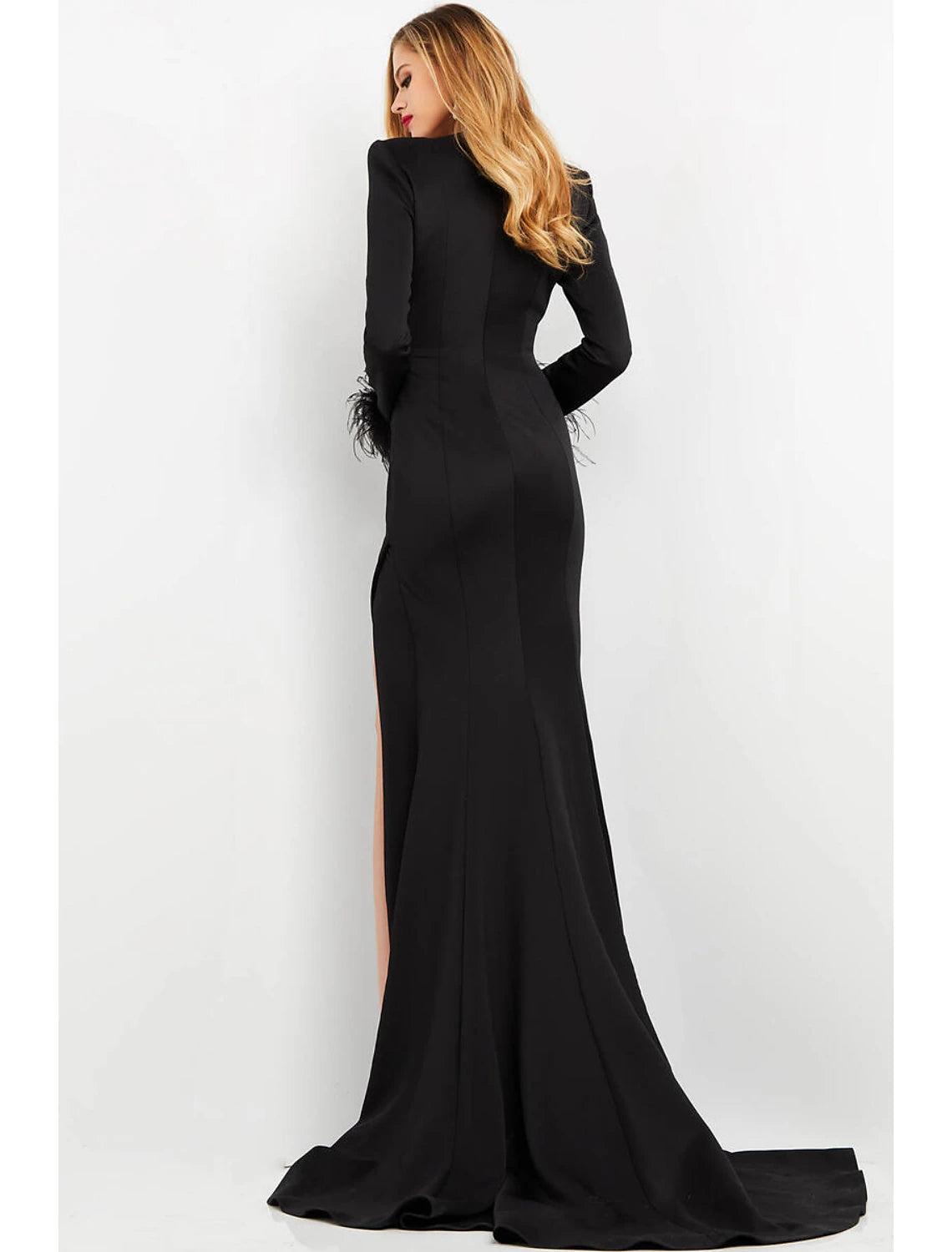Elegant woman posing in a formal long sleeve mermaid gown with a dramatic feather slit.