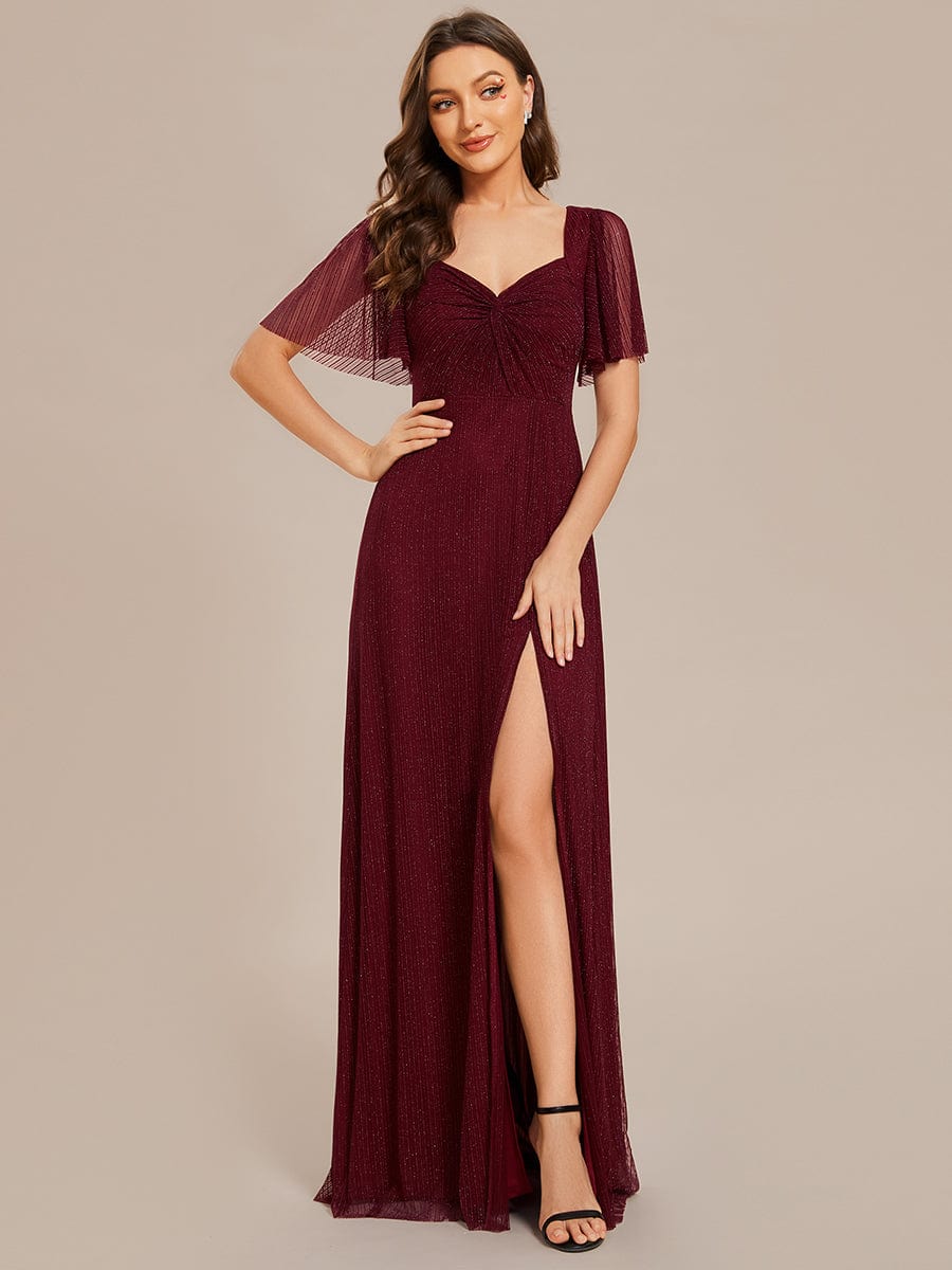 Woman wearing a glittery A-line bridesmaid dress with a high slit and short sleeves, front view.
