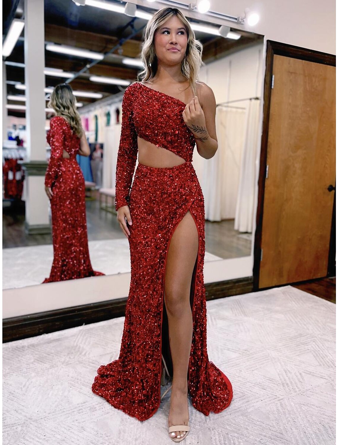 Woman wearing a sparkling one-shoulder long-sleeve mermaid prom dress with a high leg slit.