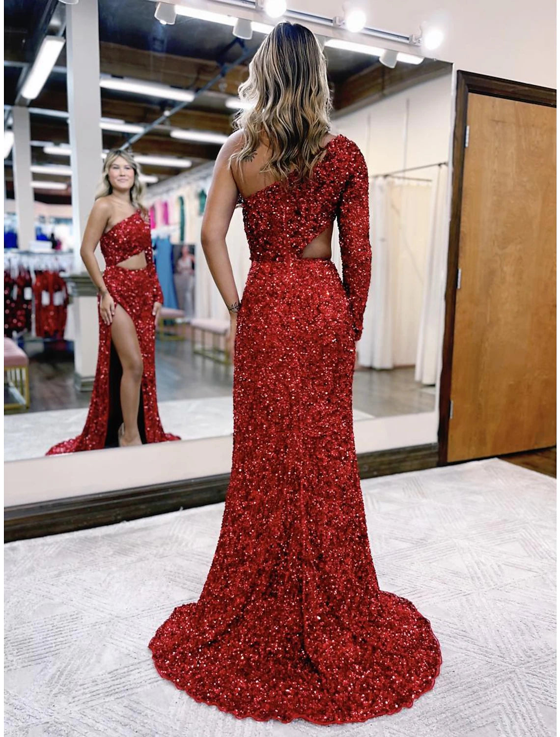 Back view of a woman in a sequined mermaid prom dress, showing the backless design and court train.