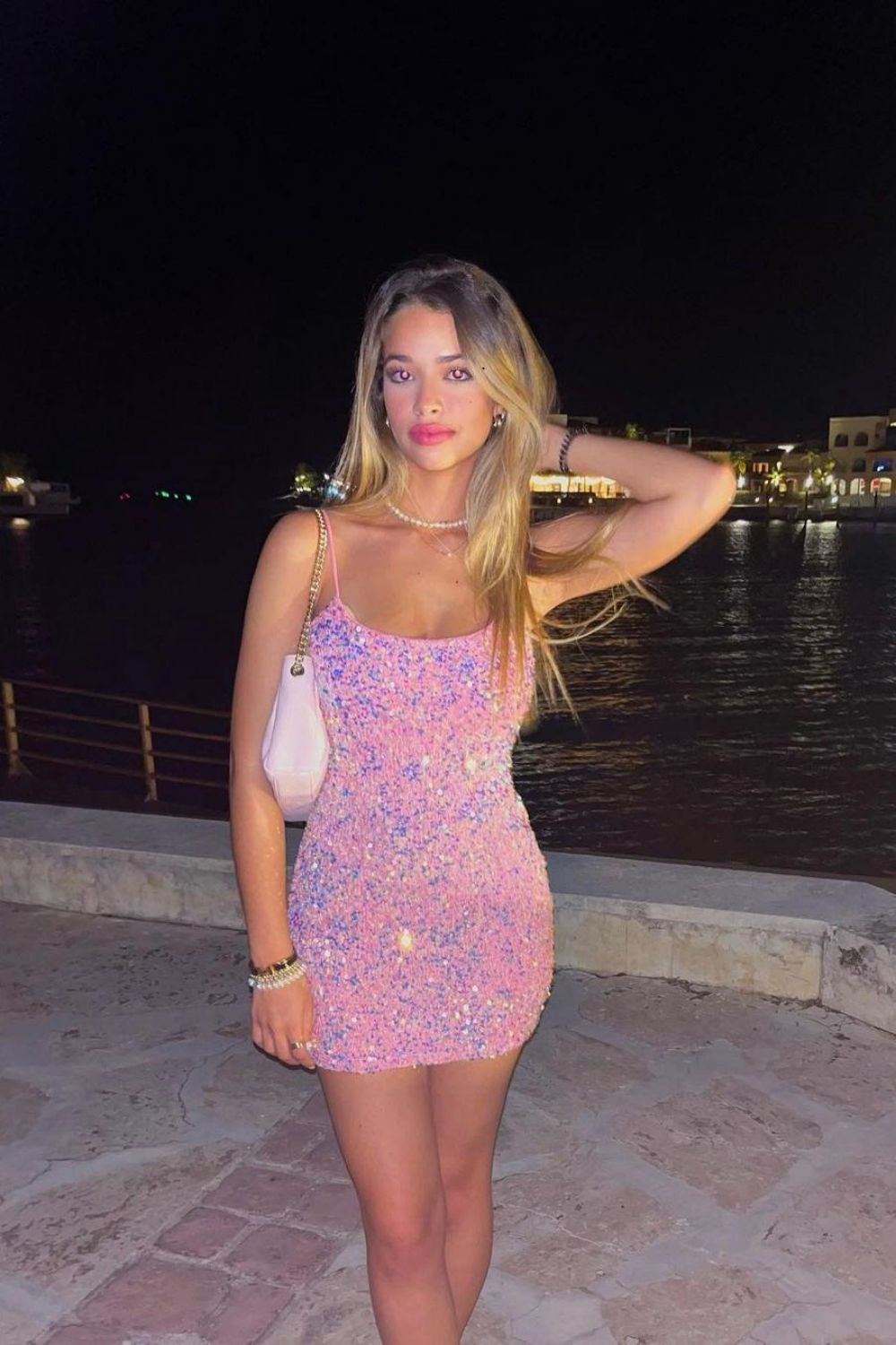 Side view of a model in a shimmering pink sequin short dress with spaghetti straps.
