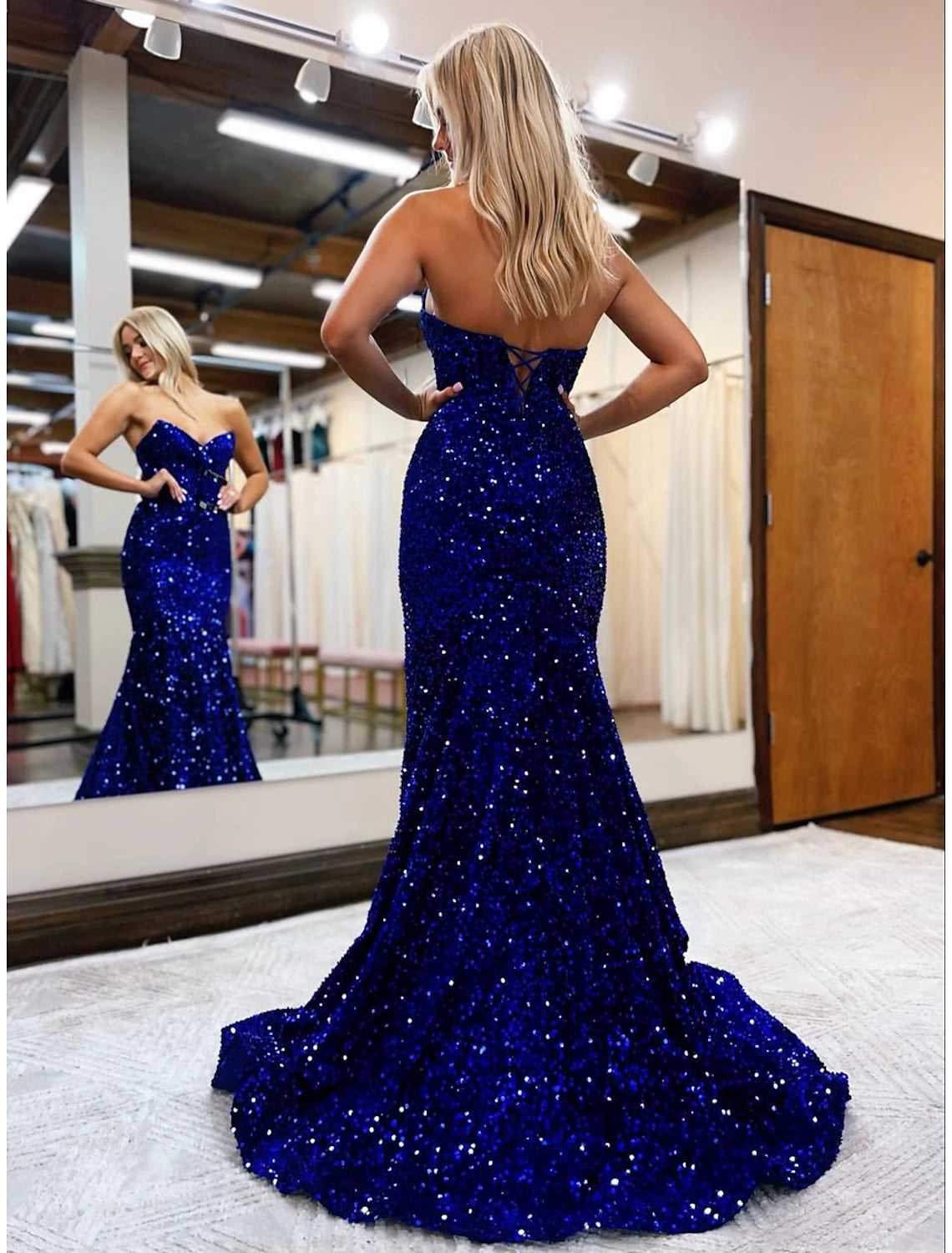 Back view of a woman wearing a sparkly sequined mermaid trumpet prom dress with a backless design and sweep train.
