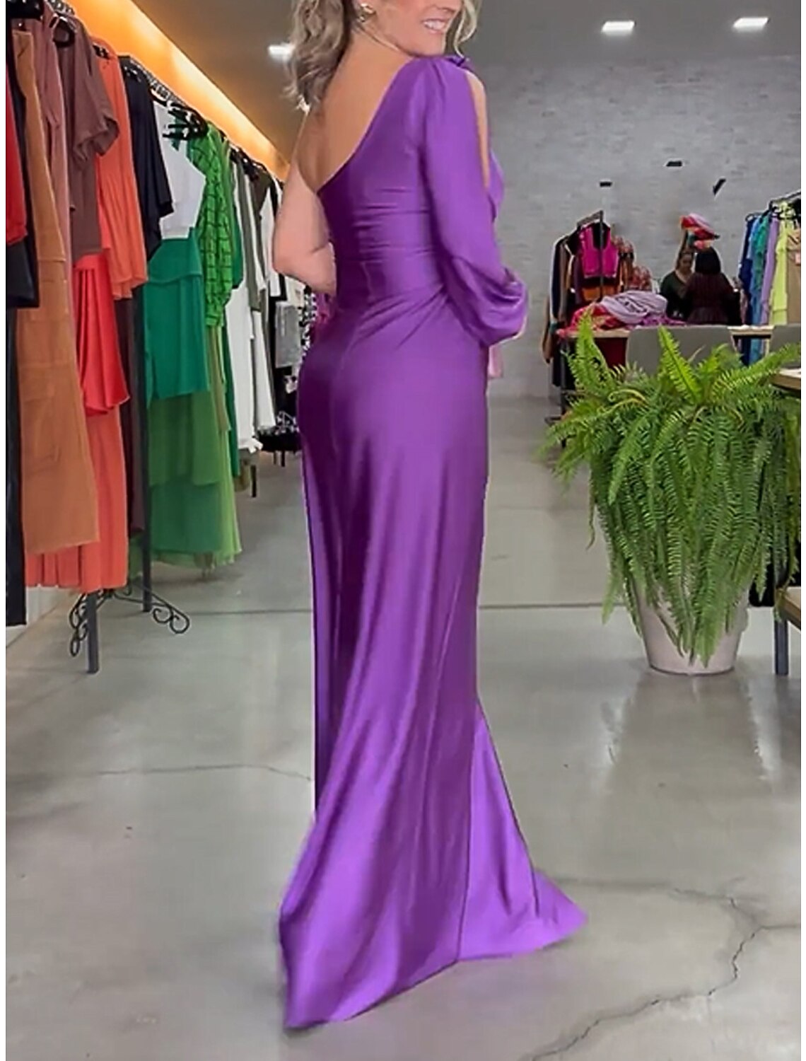 Side view of a woman in a purple one-shoulder ruched satin maxi dress, showing back detail.