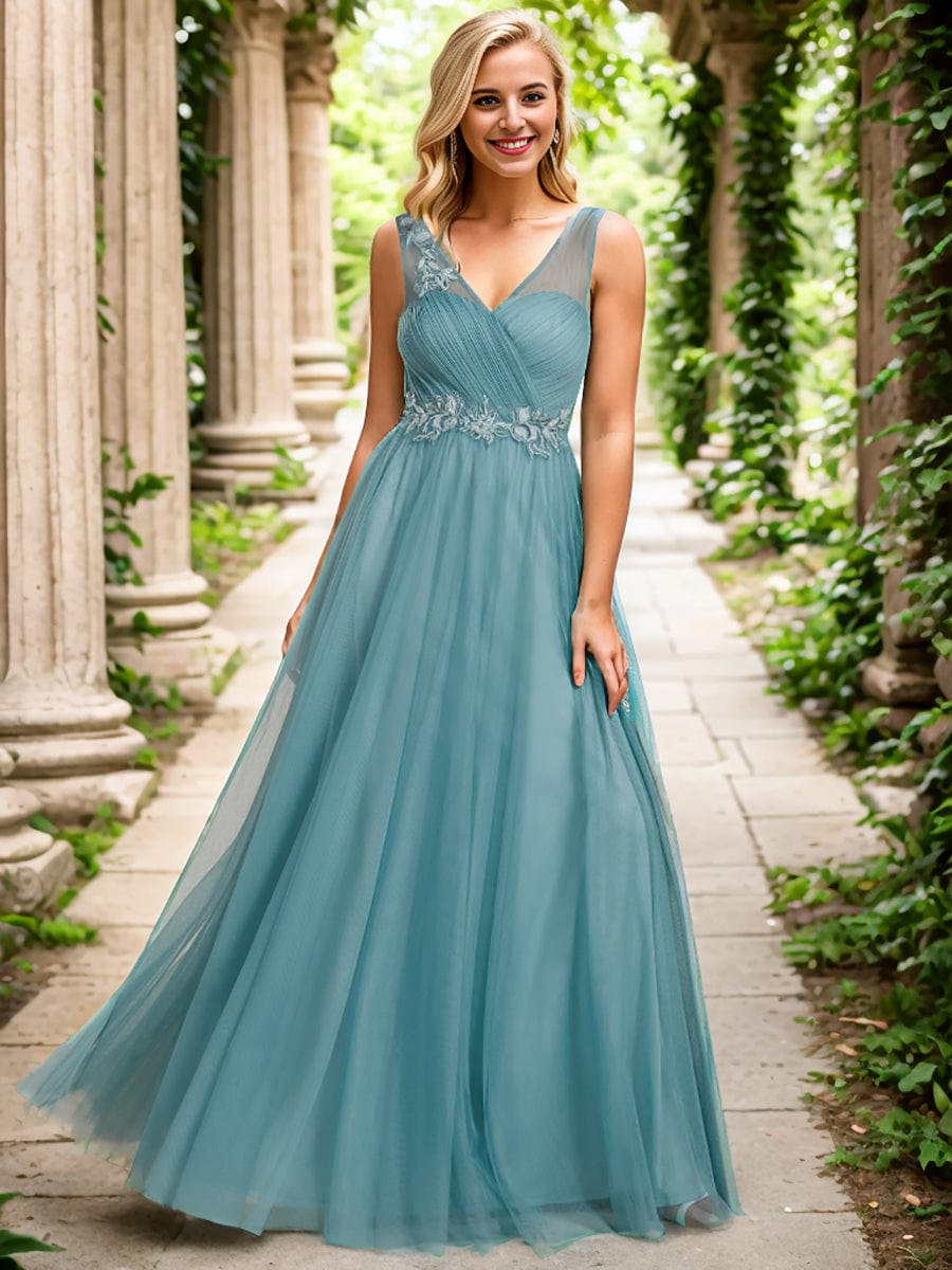 A woman wearing a dark blue Weitese sheer shoulder strap floral tulle bridesmaid dress, full length.