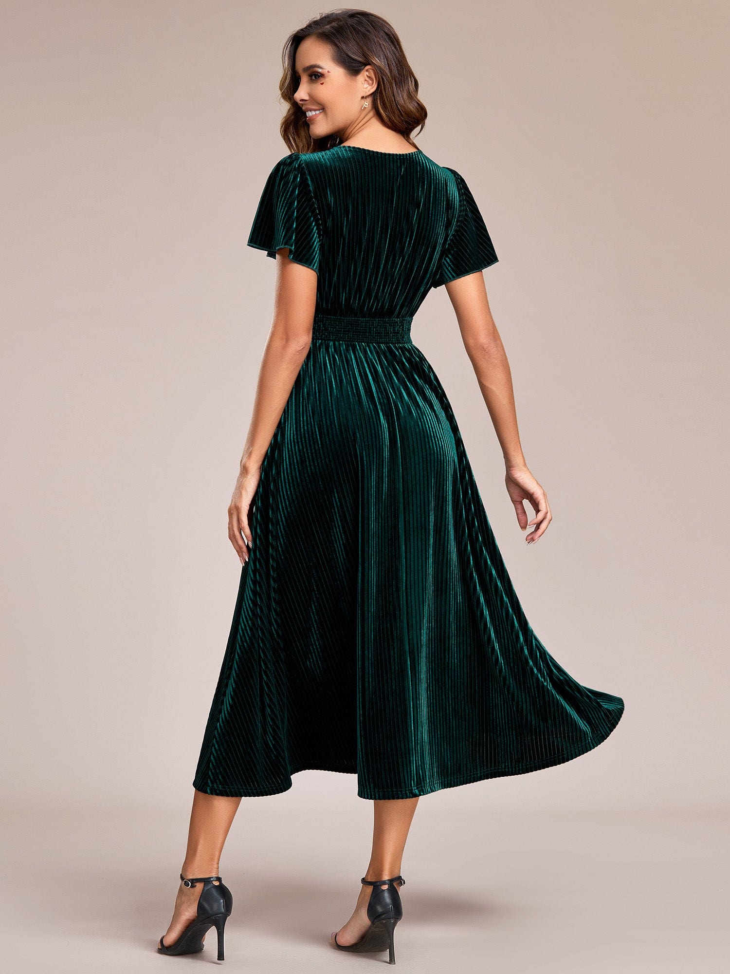 Side view of a model in a dark green velvet midi dress, highlighting the waist design.