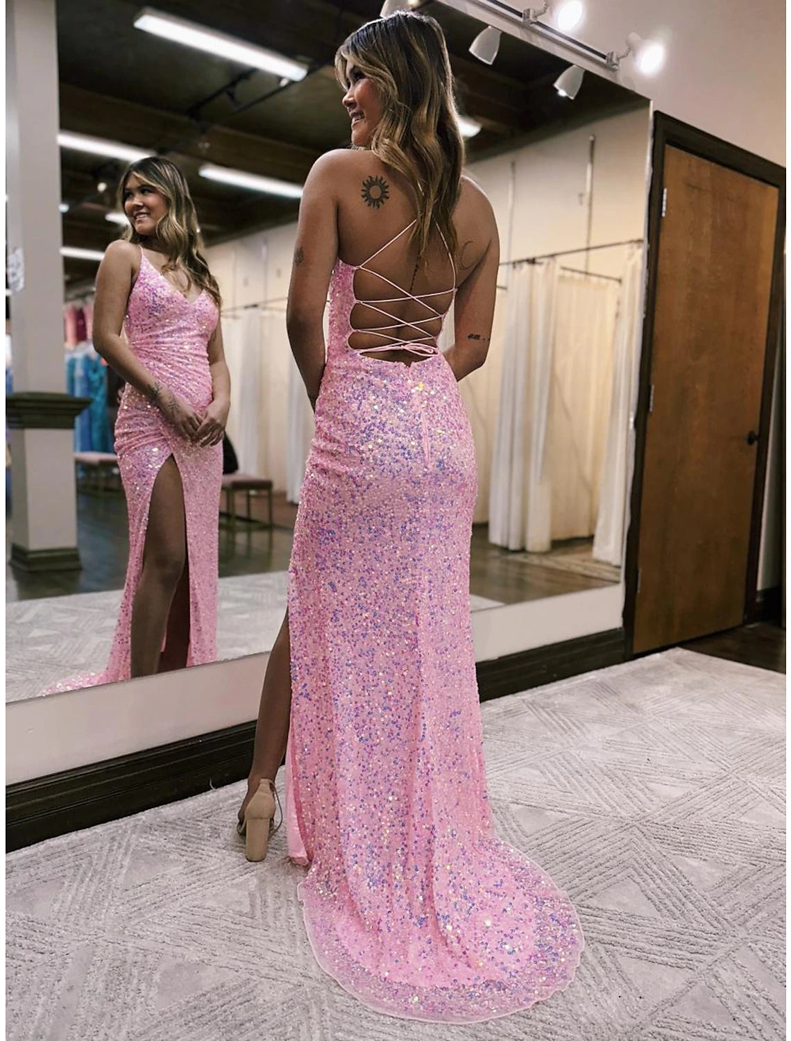 Back view of a woman in a sequined mermaid trumpet gown, showcasing the backless design and train.